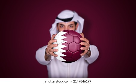 Arab man holding soccer ball in hand with Qatar flag standing on red background. - Shutterstock ID 2147846199
