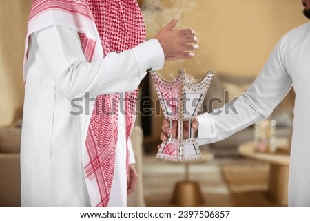 Arab man holds an incense burner and perfumes his guest with it