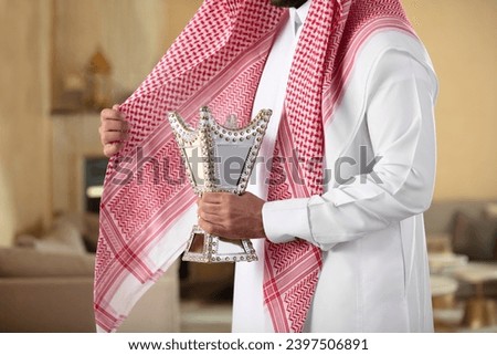 An Arab man holds an incense burner and perfumes himself with its smoke