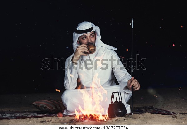 夜 砂漠で焚き火の近くに座るアラブ人の男性が 伝統的な服を着たお茶を飲む の写真素材 今すぐ編集