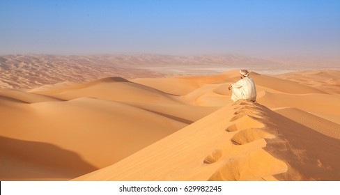 Arab man sitting on top of a dune in arabian desert