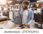 Arab man smiling while completing a purchase of jeans with nfc contactless payment using a smartphone at a retail store