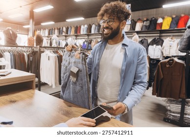 Arab man smiling while completing a purchase of jeans with nfc contactless payment using a smartphone at a retail store