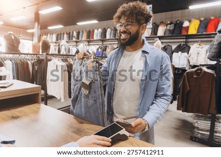 Arab man smiling while completing a purchase of jeans with nfc contactless payment using a smartphone at a retail store