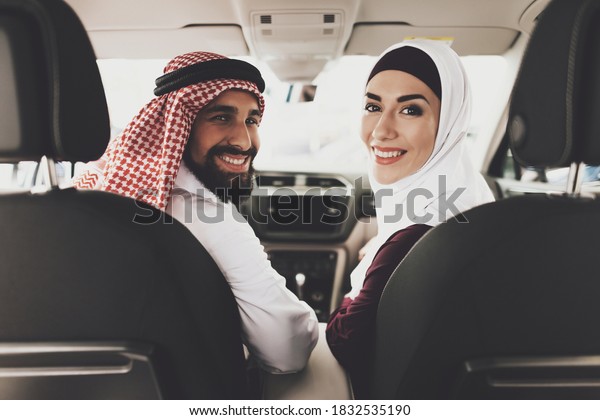 Arab man with a woman turned around and looking\
at the camera while sitting in a new car. Arab man with a beard\
looks at the camera and\
smiles.