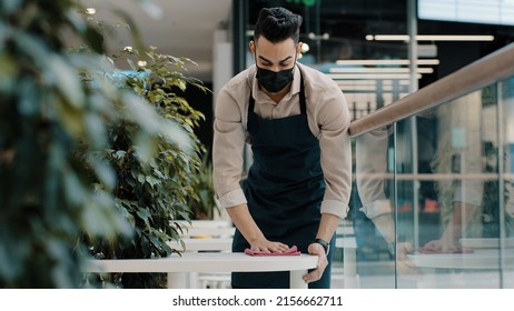 Arab Man Worker Hispanic Male Waiter In Medical Mask Catering Worker In Apron Wipes Table Splashing With Disinfectant Does Cleaning Before Opening Restaurant Prepares Cafe For Open Visitors Works