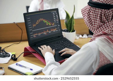 Arab man working on laptop in the office, watching stock market