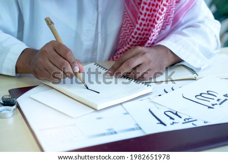 Arab men practicing writing Arabic  with bamboo pens and ink on paper, Arabic letters mean the name of Muslim god 