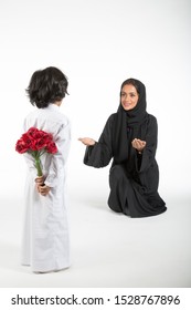 Arab middle eastern Saudi Boy with flowers behind his back, surprising his mom on mother’s day, on white isolated background, ready for cutout and design purposes.