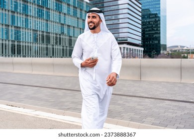 Arab middle-eastern man wearing emirati kandora traditional clothing in the city - Arabian muslim businessman strolling in urban business centre.