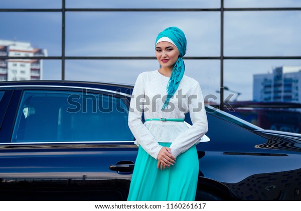 Arab Muslim business woman\
hijab with makeup standing in front of her luxury car on the street\
on a background of skyscrapers . The woman is dressed in a stylish\
abaya