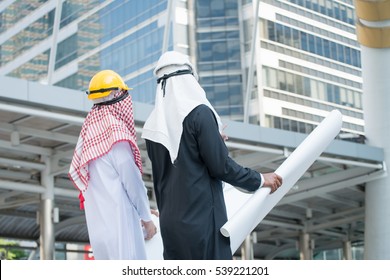 Arab Muslim Engineer And Worker Checking Construction Drawing At Construction Site.