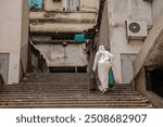 Arab or muslim woman is walking up a long set of stairs in dirty environment. Typical view of a city in Oran, Algeria. Frequently used stairs but neglected, covered in filth