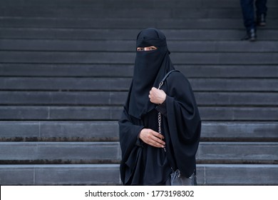 Arab Muslim woman wearing a black niqab in front of the stairs, looking at camera