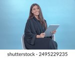 Arab Saudi or Emirati woman wearing Abaya using tablet working or reading. Arabian brunette girl happy thumbs up on blue background