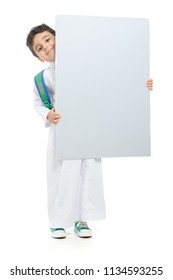 Arab school boy raising a big white board with both hands, wearing white traditional Saudi Thobe and sneakers, raising his hands on white isolated background