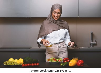 Arab Wife Cooking In Kitchen, Making Fresh Vegetable Salad With Olive Oil Dressing Standing At Home, Wearing Hijab. Happy Arab Lady Preparing Healthy Dinner Meal Indoor. Arabic Cuisine, Recipes