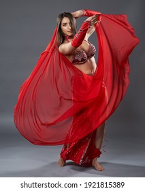 Arab woman belly dancer in red sparkling costume on gray background