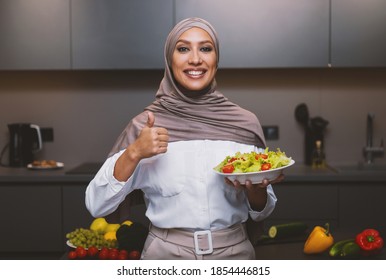 Arab Woman Holding Salad Bowl Gesturing Thumbs Up Approving Recipe Cooking In Kitchen Indoor, Posing Smiling To Camera. Great Dinner Recipe, I Like To Cook Healthy Meals Concept