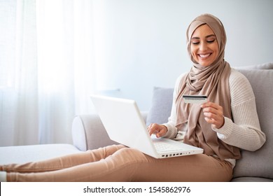 Arab Woman Making Online Purchase On Laptop. Portrait Of Happy Woman Purchasing Product Via Online Shopping. Pay Using Credit Card. Muslim Woman Online Shopping