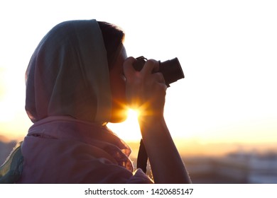 Arab Woman Photographer in a scarf taking picture using Camera on the sunset background. Halal travel concept  - Powered by Shutterstock