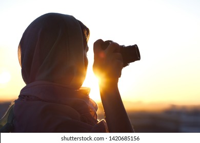 Arab Woman Photographer in a scarf taking picture using Camera on the sunset background. Halal travel concept  - Powered by Shutterstock