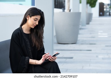 Arab Woman Sitting Wearing Abaya In A Business Background. Arabian Female Shopping Online Carrying Mobile Phone Or Working In Traditional Dress