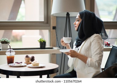 Arab Women In Hijab Holding And Drinking Coffee Cup Sitting In The Coffee Shop.