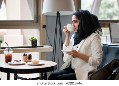 Arab women in hijab holding and drinking coffee cup sitting in the coffee shop. - Powered by Shutterstock