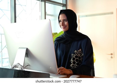 Arab at work. Natural sunlights brights the office environment. Emirati woman using computer screen typing on the keyboards. Girl in Abaya and Hijab
