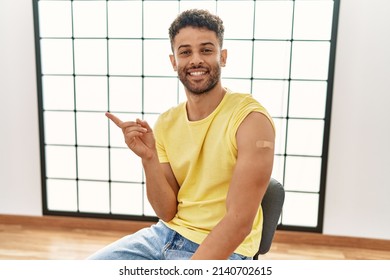 Arab Young Man Getting Vaccine Showing Arm With Band Aid Smiling Happy Pointing With Hand And Finger To The Side 