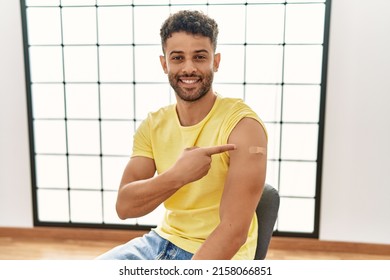 Arab Young Man Getting Vaccine Showing Arm With Band Smiling Happy Pointing With Hand And Finger 