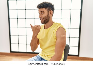 Arab Young Man Getting Vaccine Showing Arm With Band Aid Pointing Thumb Up To The Side Smiling Happy With Open Mouth 