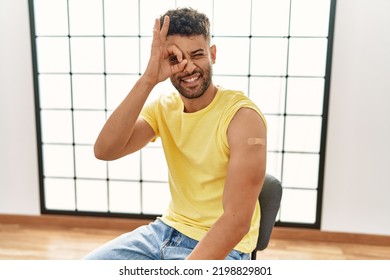 Arab Young Man Getting Vaccine Showing Arm With Band Aid Smiling Happy Doing Ok Sign With Hand On Eye Looking Through Fingers 