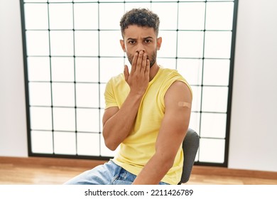 Arab Young Man Getting Vaccine Showing Arm With Band Aid Covering Mouth With Hand, Shocked And Afraid For Mistake. Surprised Expression 