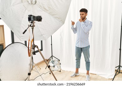 Arab Young Man Posing As Model At Photography Studio Asking To Be Quiet With Finger On Lips Pointing With Hand To The Side. Silence And Secret Concept. 