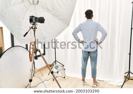 Arab young man posing as model at photography studio standing backwards looking away with arms on body 
