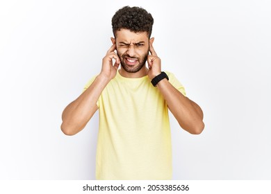 Arab Young Man Standing Over Isolated Background Covering Ears With Fingers With Annoyed Expression For The Noise Of Loud Music. Deaf Concept. 