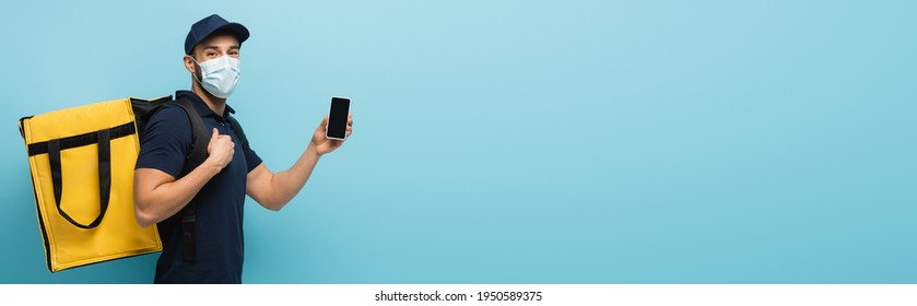 Arabian Delivery Man In Medical Mask Showing Smartphone With Blank Screen On Blue, Banner