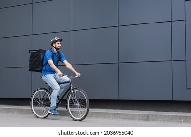 Arabian deliveryman with backpack riding bicycle near building
