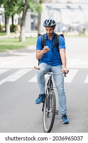 Arabian deliveryman with backpack using smartphone while riding bicycle outdoors