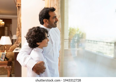 Arabian father embracing son at home  looking at the window 