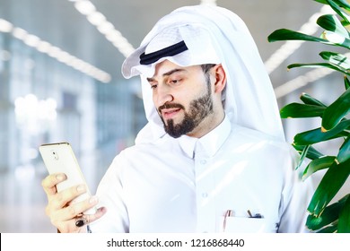 Arabian (Gulf Area) Smiling Man With Traditional Wear And Using A Mobile Phone.