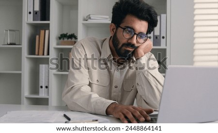 Arabian Indian ethnic male tired businessman office employee boring work with laptop dreary exhausted lazy bored business man low energy overworked fatigue depression apathy burnout typing on computer