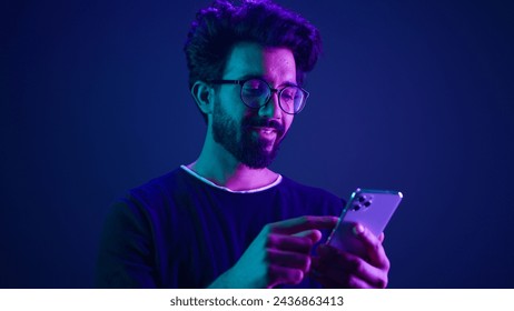 Arabian male using mobile phone chatting browsing smartphone online order shopping gaming with cellphone Indian man scrolling social media internet technology app at neon ultraviolet studio background