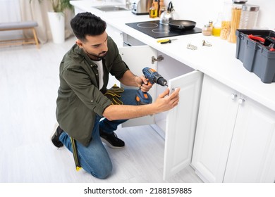 Arabian man with electric screwdriver fixing cabinet under worktop in kitchen - Shutterstock ID 2188159885