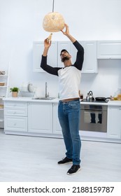 Arabian Man Holding Lightbulb Near Chandelier In Kitchen