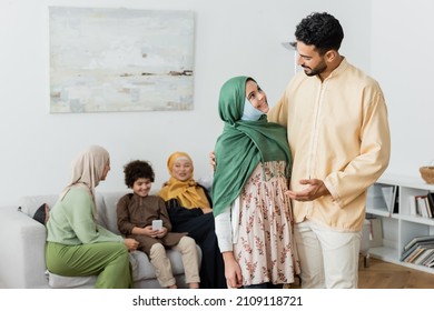 arabian man talking to muslim daughter near multiethnic family on blurred background