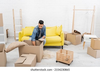 Arabian man unpacking package near boxes and bengal cat at home - Powered by Shutterstock