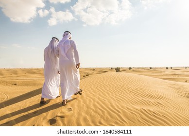Arabian men witk kandora walking in the desert - Portrait of two middle eastern adults with traditional arabic dress
